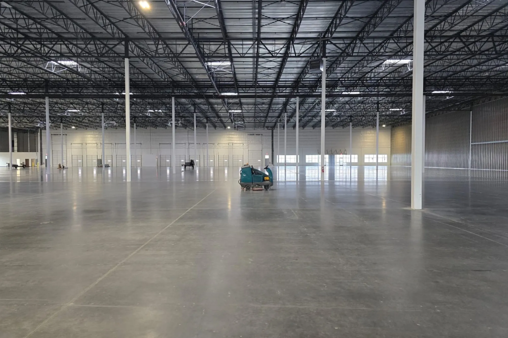 Ride-on floor scrubber cleaning the concrete floor of an empty warehouse