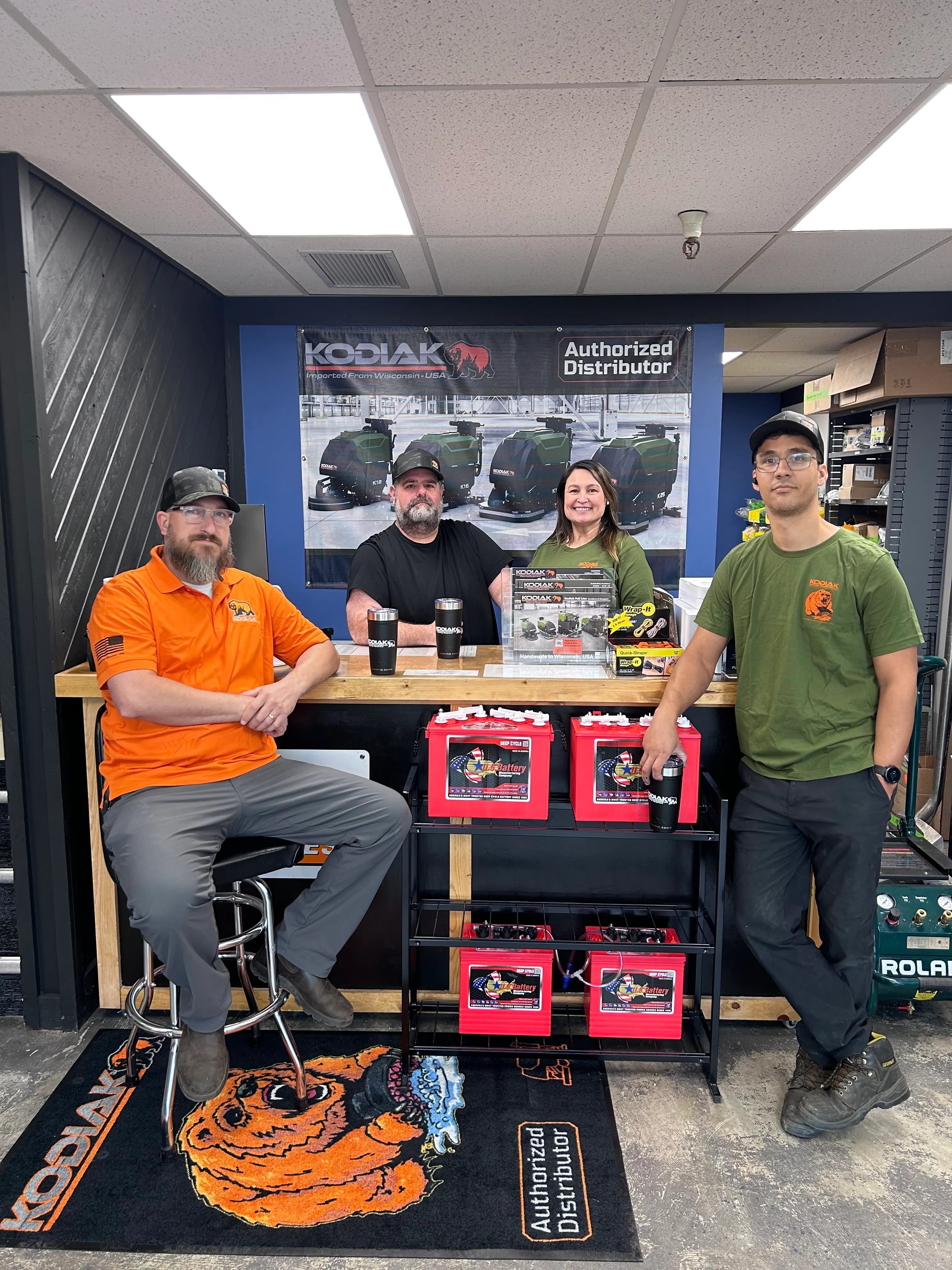 Four Advance Cleaning Equipment team members in the Boise shop with a Kodiak Authorized Distributor banner and U.S. Battery deep-cycle batteries